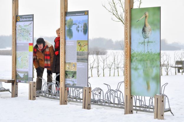 Twee wandelaars kijken op de informatieborden in het winterse landschap van Greenspot Schulensbroek op de grens van Herk-de-Stad, Lummen en Halen