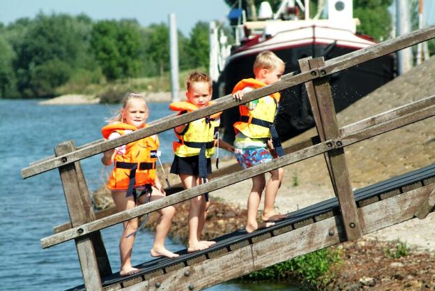 Drie kinderen op de loopbrug van een boot in Kinrooi, klaar voor een tocht over de Maas