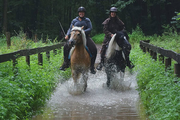 Twee amazones draven met hun paarden door de doorwaadplaats in Oudsbergen